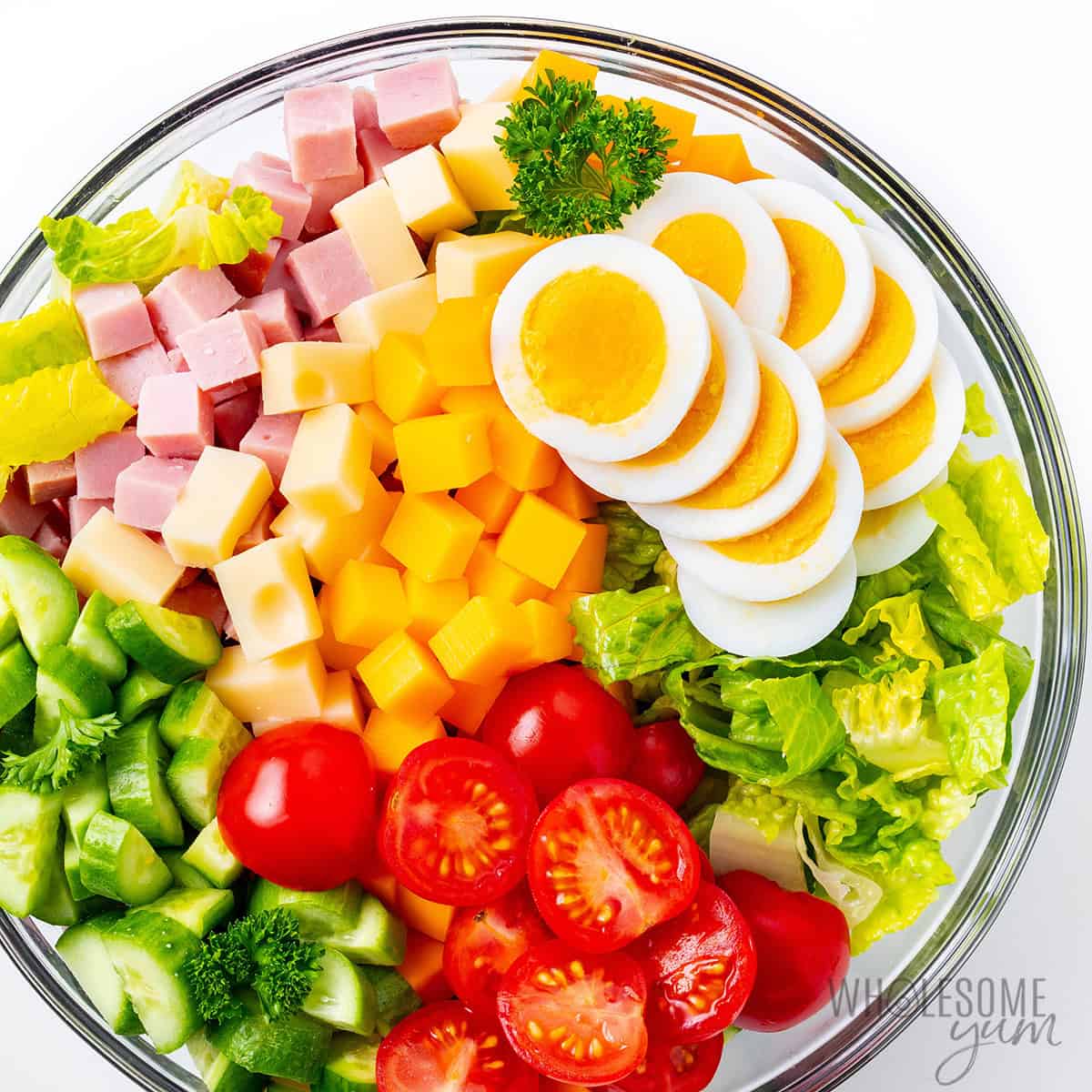 Lettuce, veggies, cheeses, ham, and eggs assembled in a large bowl.
