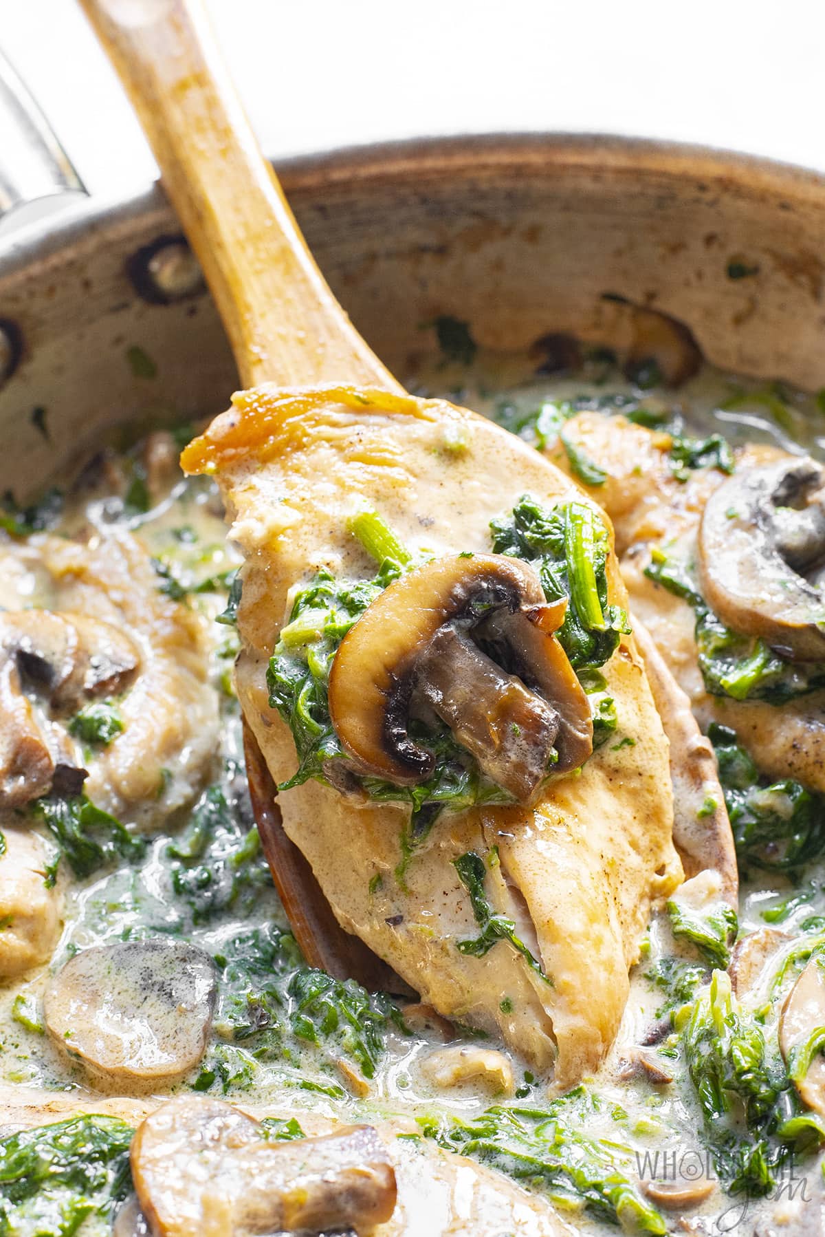 Chicken Florentine recipe scooped out of pan with a wooden spoon.