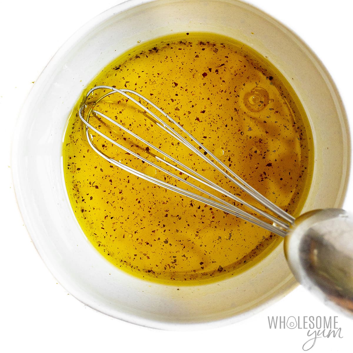 Dressing ingredients in a bowl with whisk.