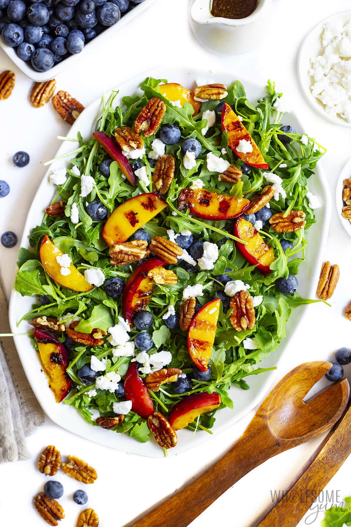 Grilled peach salad recipe next to serving spoons and berries.