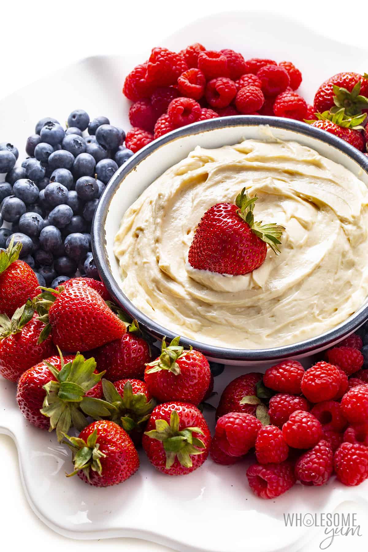 Keto fruit dip in a bowl with berries plated around it.