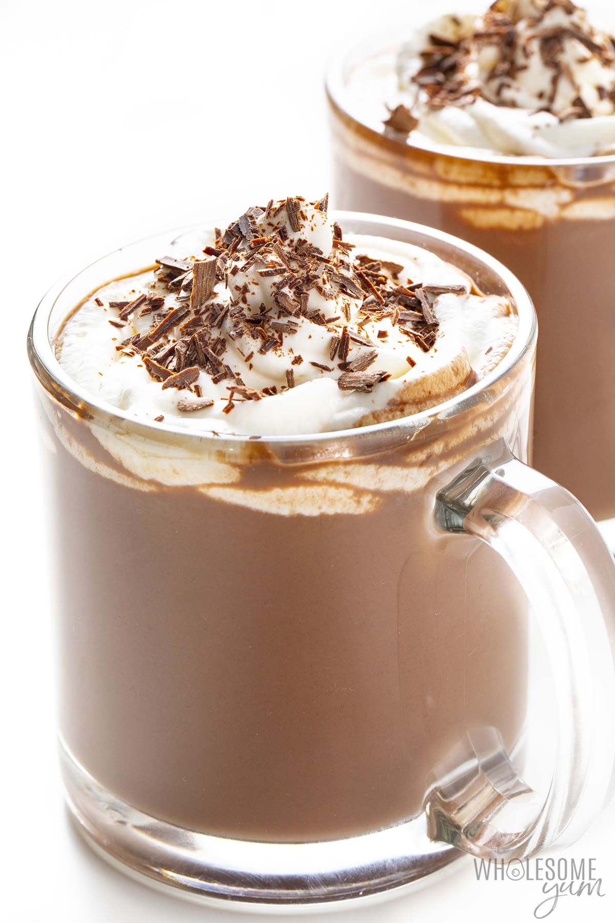 Hot chocolate in 2 mugs with whipped cream and chocolate on top.