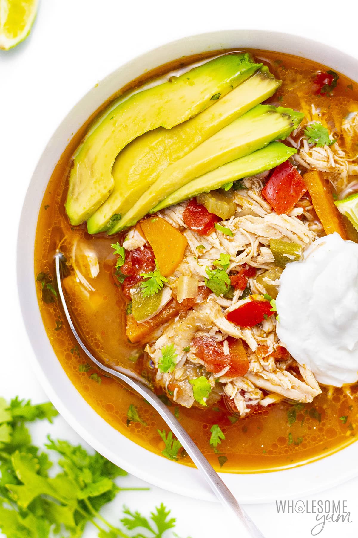 Bowl of Mexican chicken soup with sliced avocado and sour cream scoop.