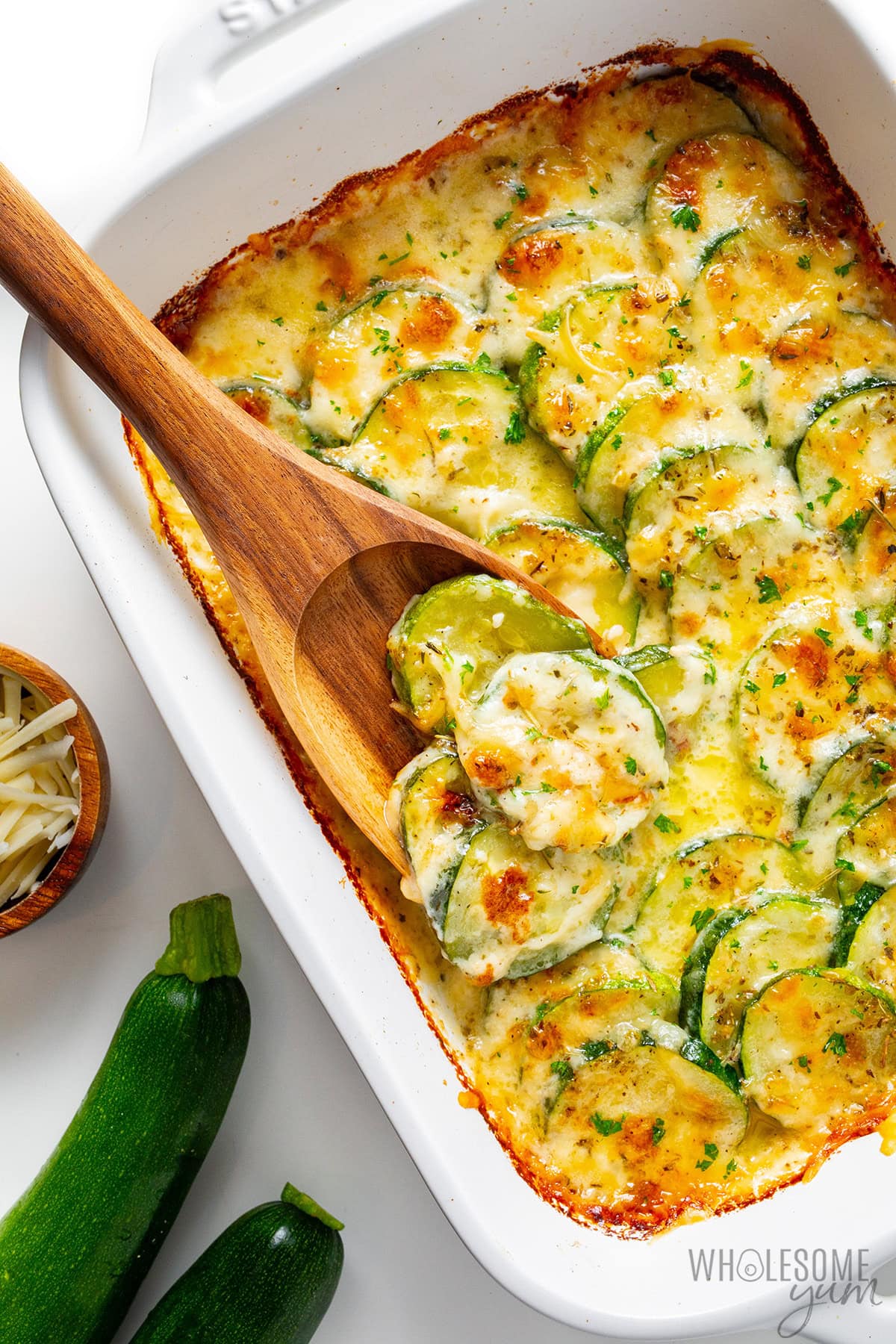 Creamy, cheesy zucchini casserole in a baking dish with a wooden spoon.