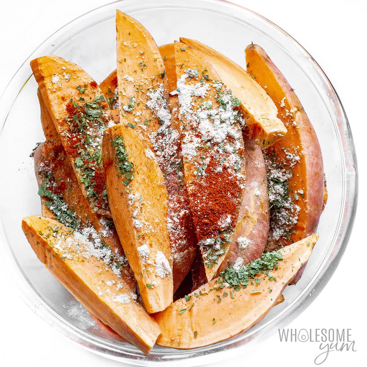 Raw sweet potatoes in a bowl with seasonings.