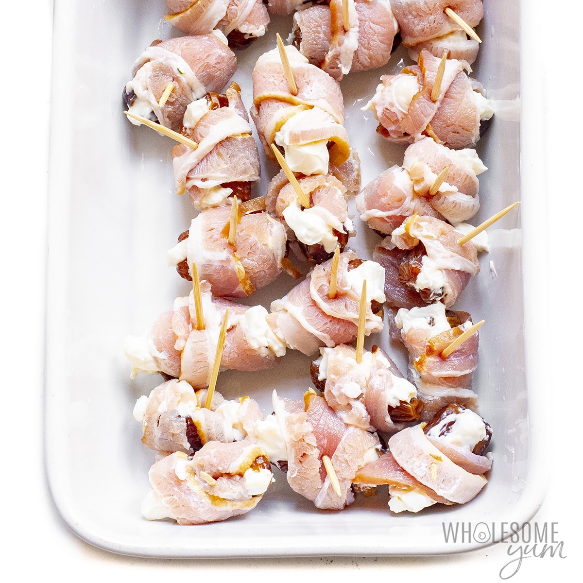 Dates wrapped in bacon in a baking dish.