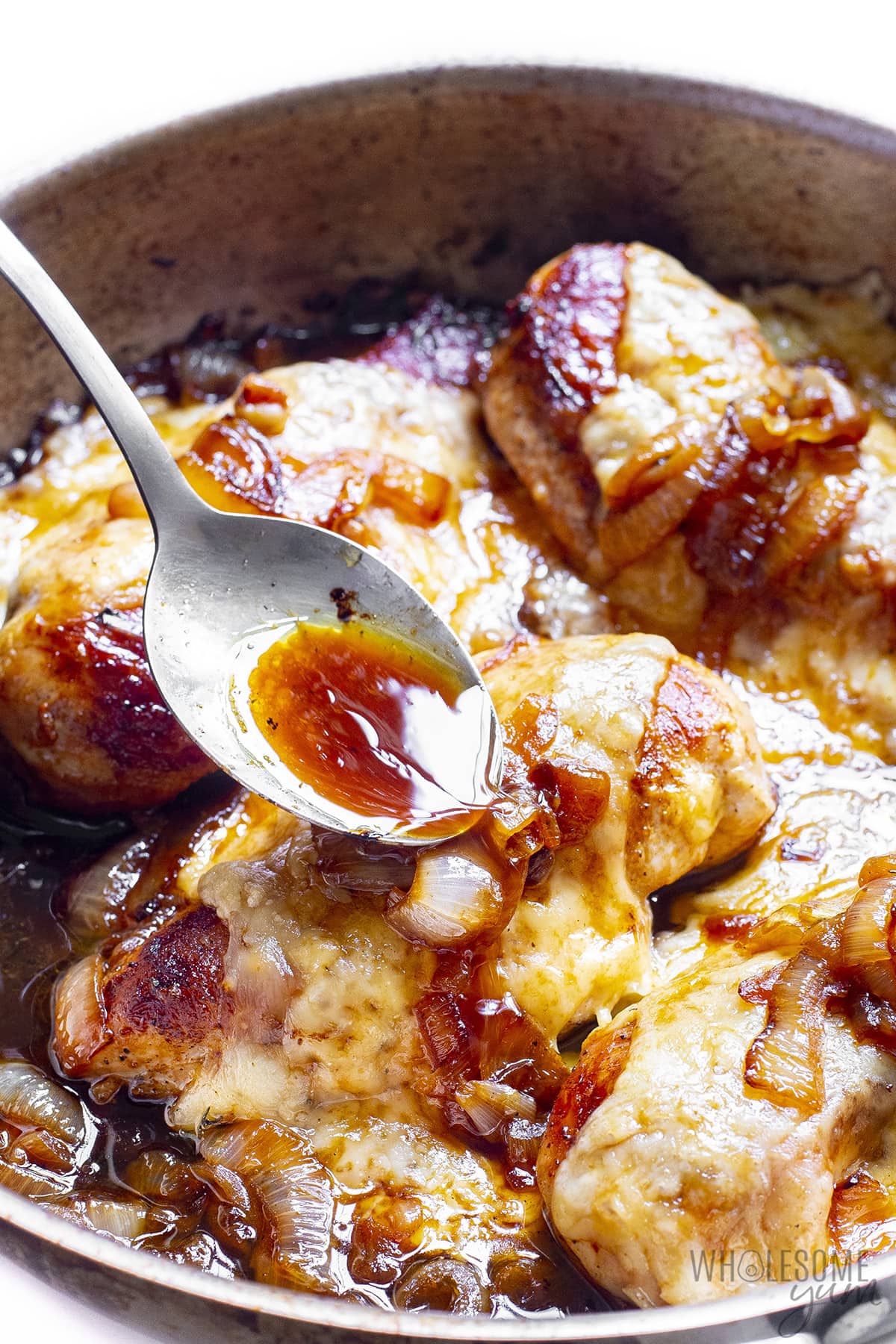 French Onion Chicken is baked in a pan with a spoon drizzled with sauce.