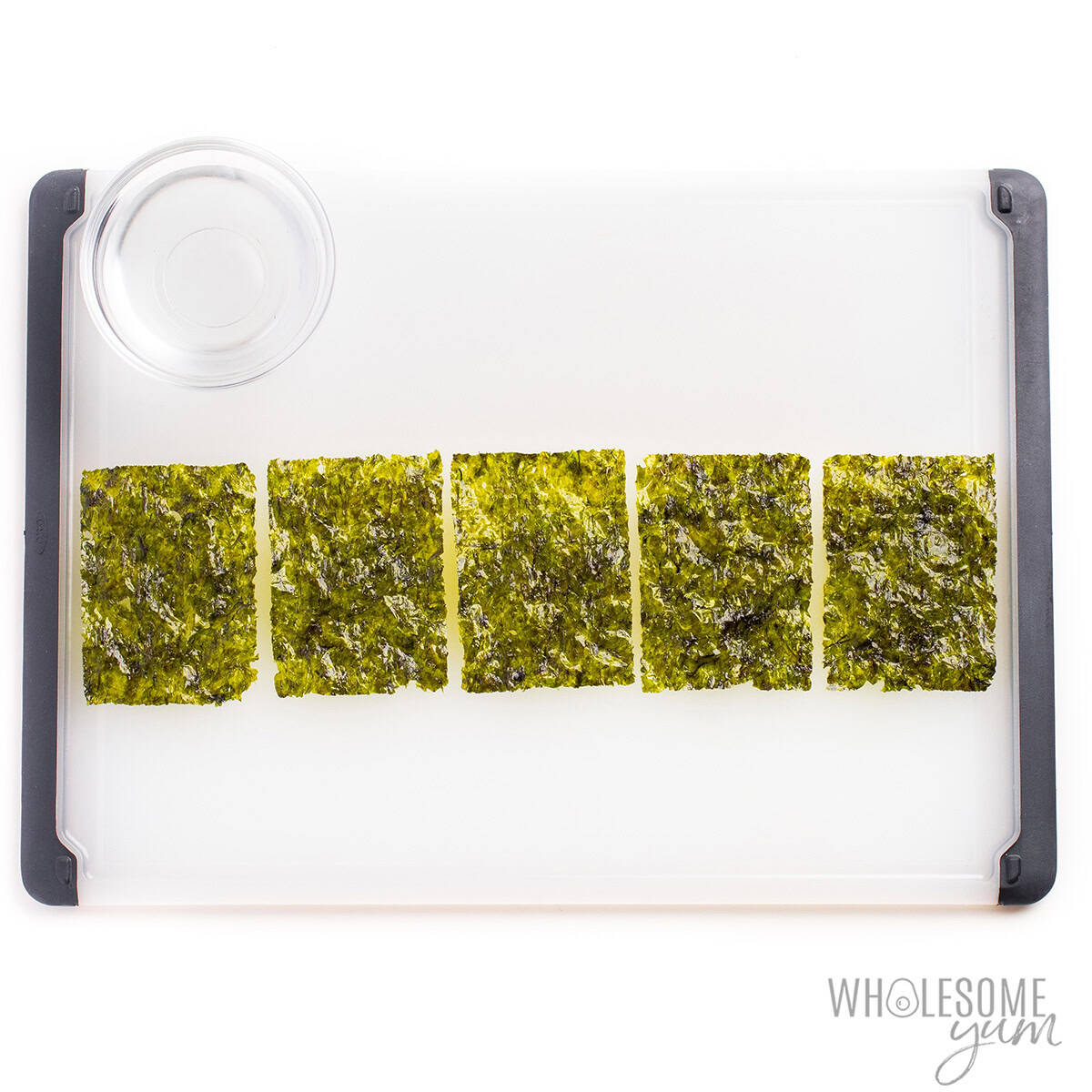 Seaweed sheets laid out on a cutting board next to a small bowl of water.