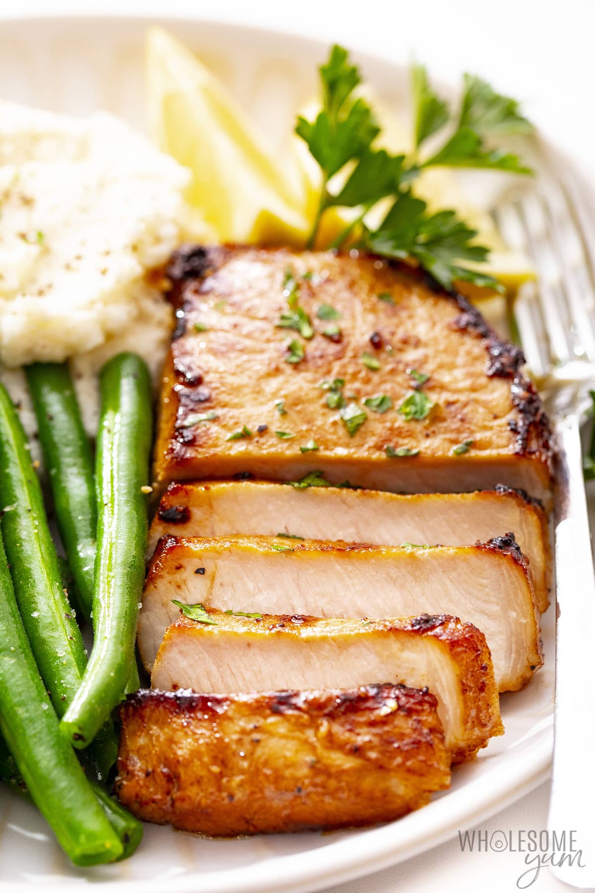 Baked pork chop recipe sliced on a plate, with green beans and mash.