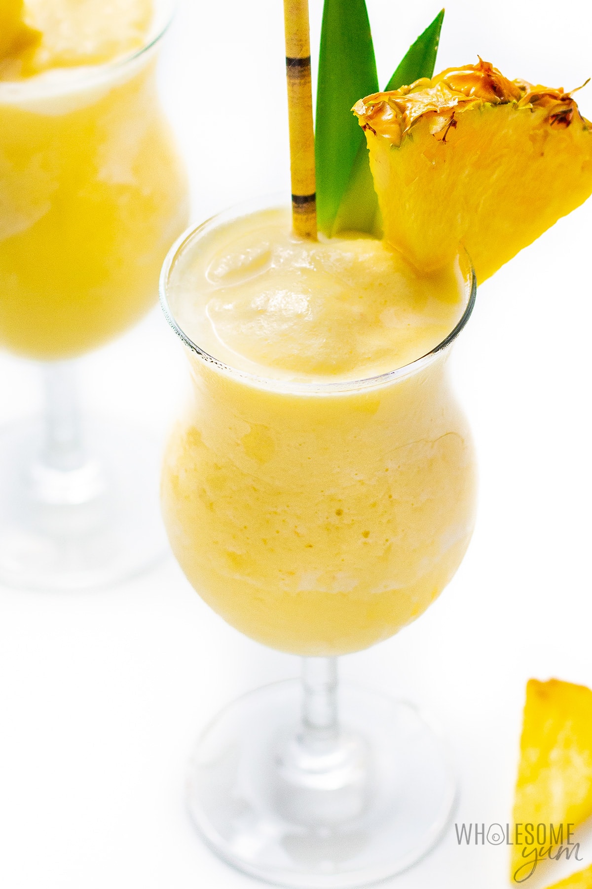 Two glasses of frozen pina colada with fresh pineapple garnishes.