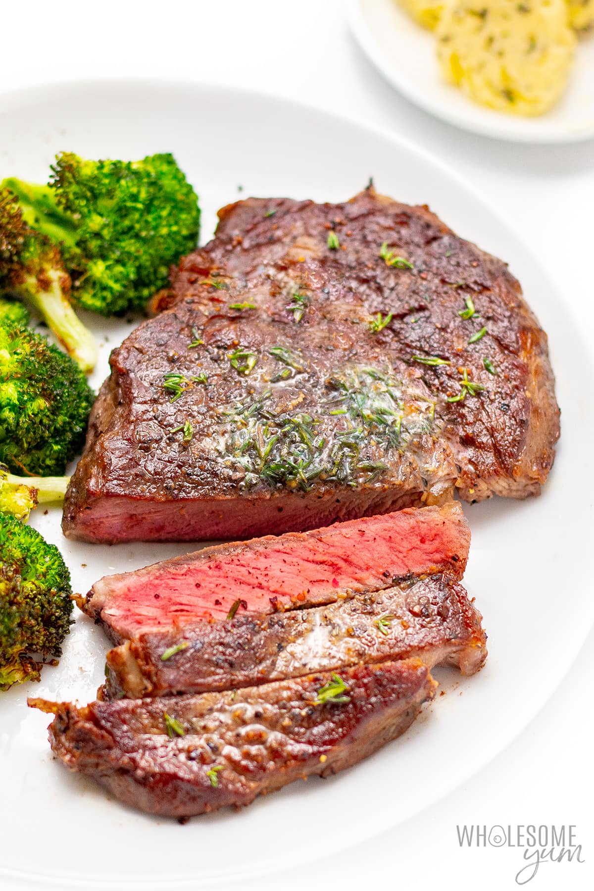 Beef chuck eye steak next to broccoli on a plate.