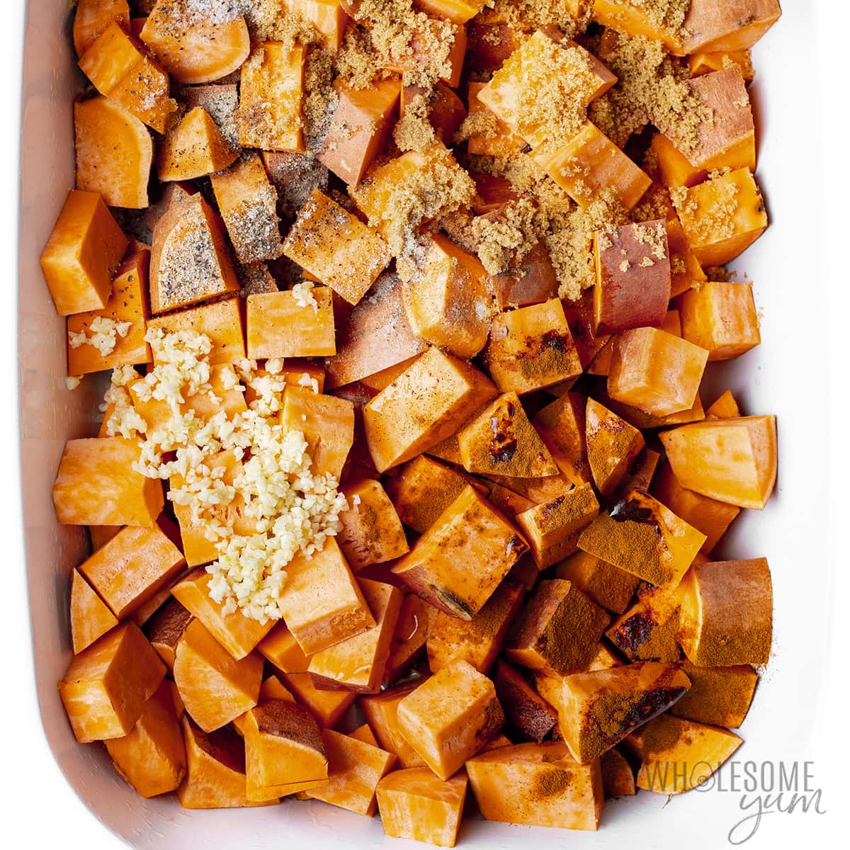 Seasonings and spices on top of cubed sweet potatoes in a baking dish. 