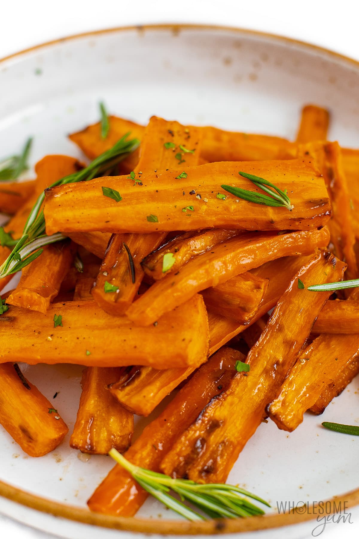 Air fryer carrots on a plate, sprinkled with rosemary. 