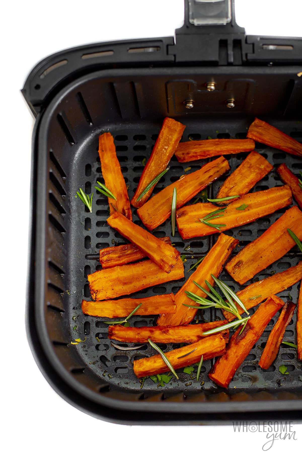Cooked carrots in air fryer basket with herbs. 
