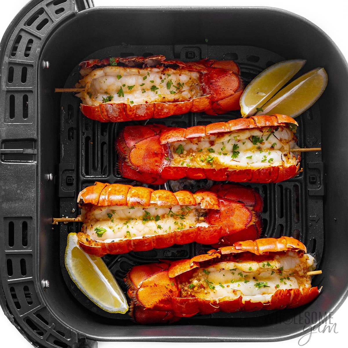 Cooked lobster tails in air fryer basket.