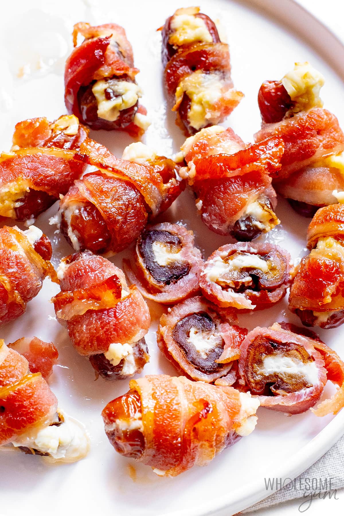 Bacon wrapped stuffed dates on a plate, with 2 cut open.