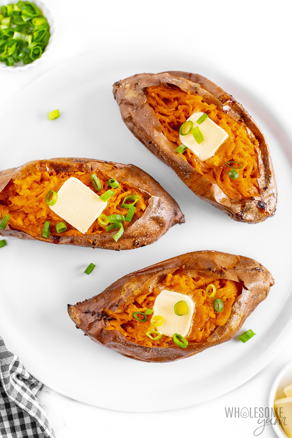 3 finished baked sweet potatoes with butter and green onions on a serving plate.