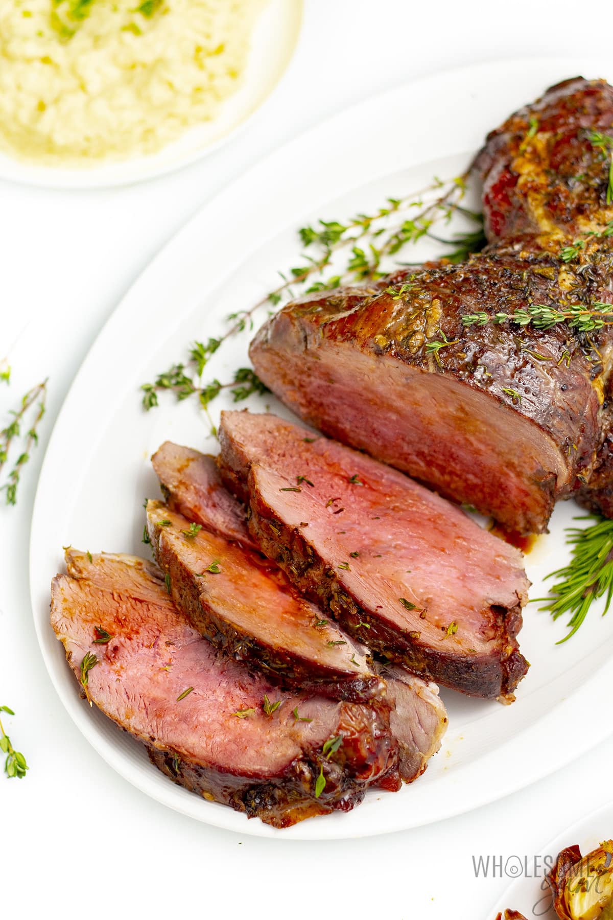 Sliced boneless leg of lamb on a serving platter with herb garnish.