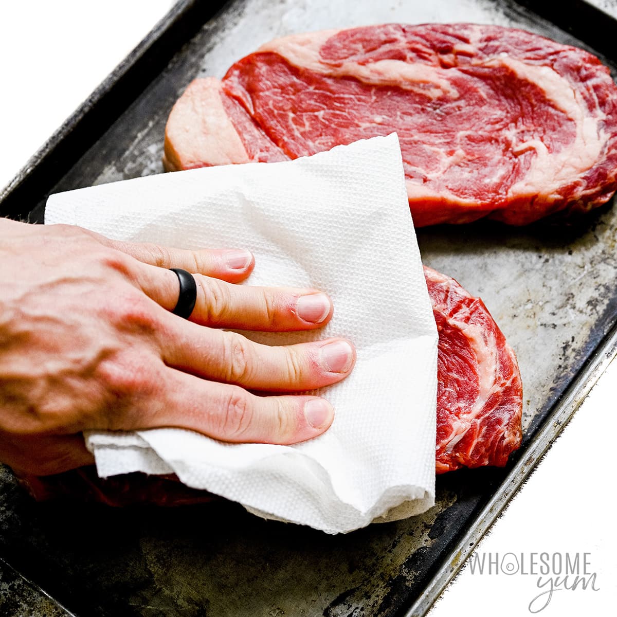 Raw steak being patted dry with paper towel.