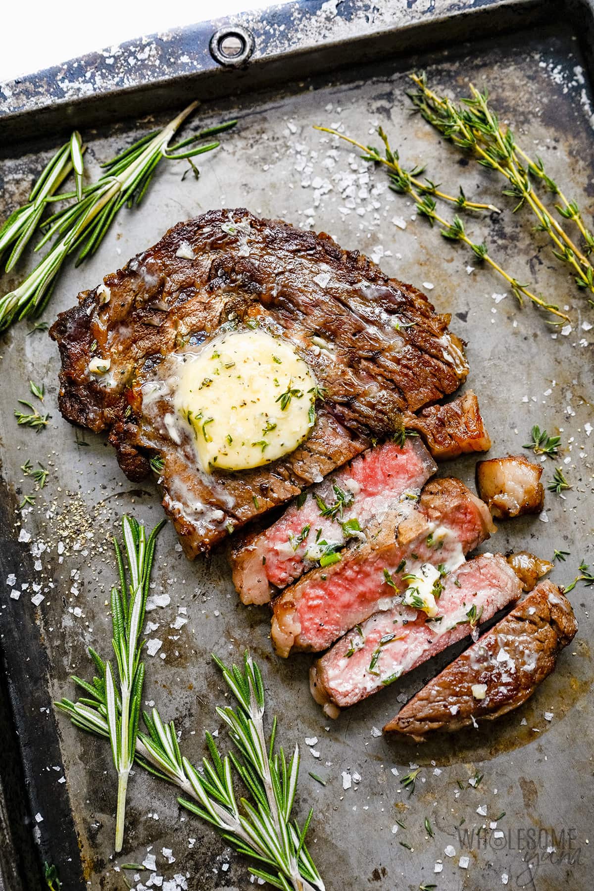 Cast Iron Ribeye Steaks smothered in melted compound butter on a griddle.