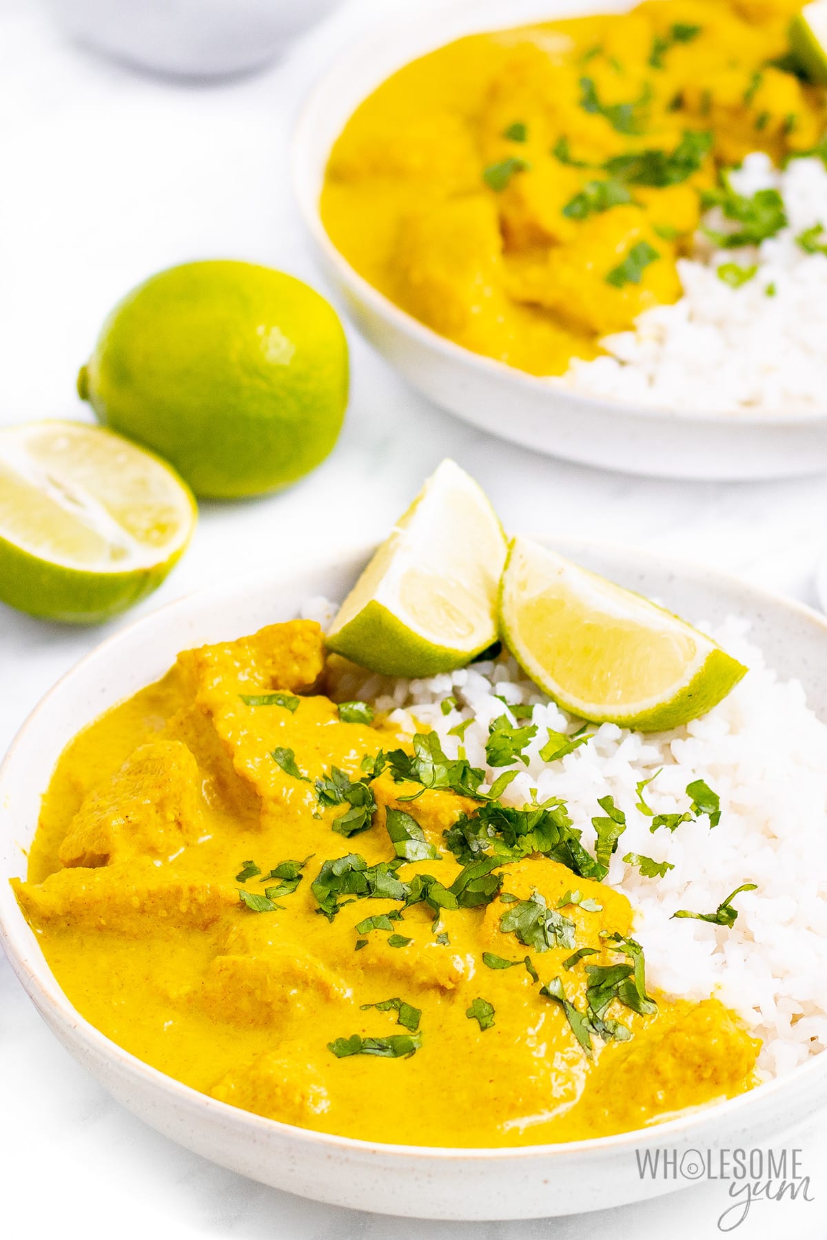 Chicken korma in bowls with limes and rice.