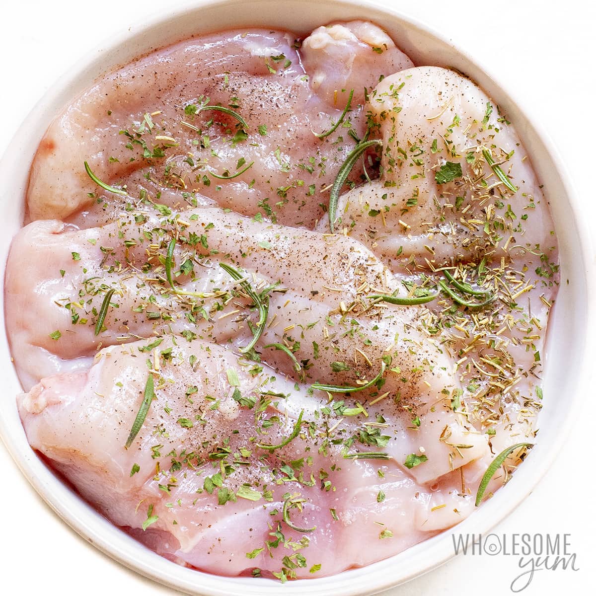 Raw seasoned chicken breasts in a bowl.