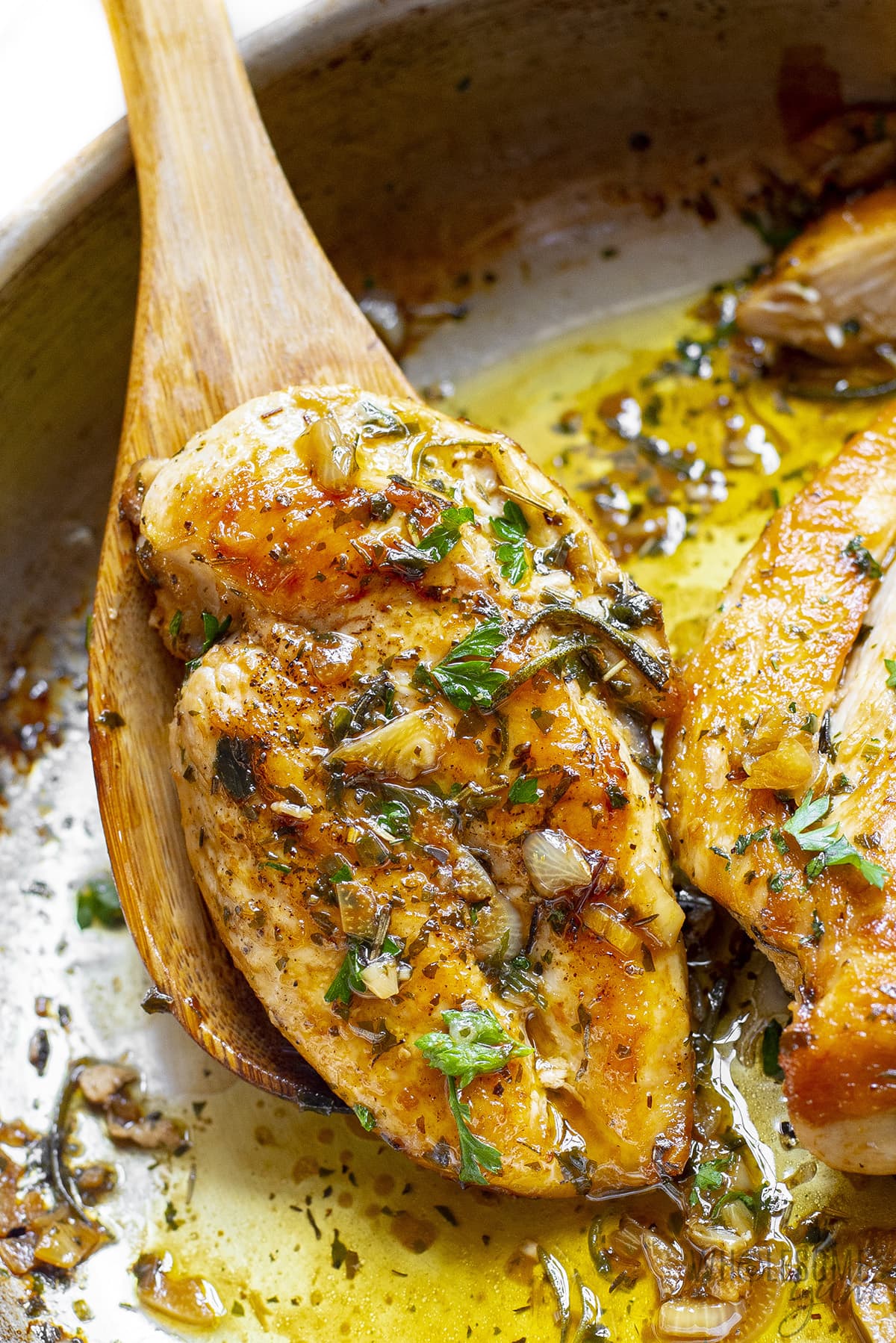 Juicy garlic butter chicken breast lifted with a wooden spoon and garnished with fresh herbs.