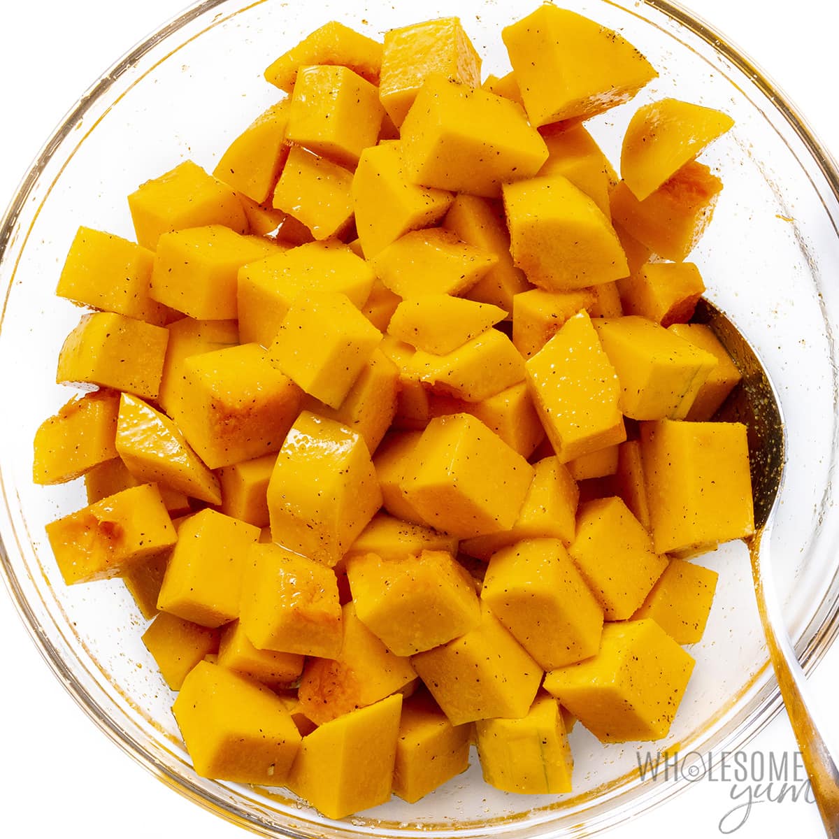 Cubes of seasoned butternut squash in a bowl with a spoon.