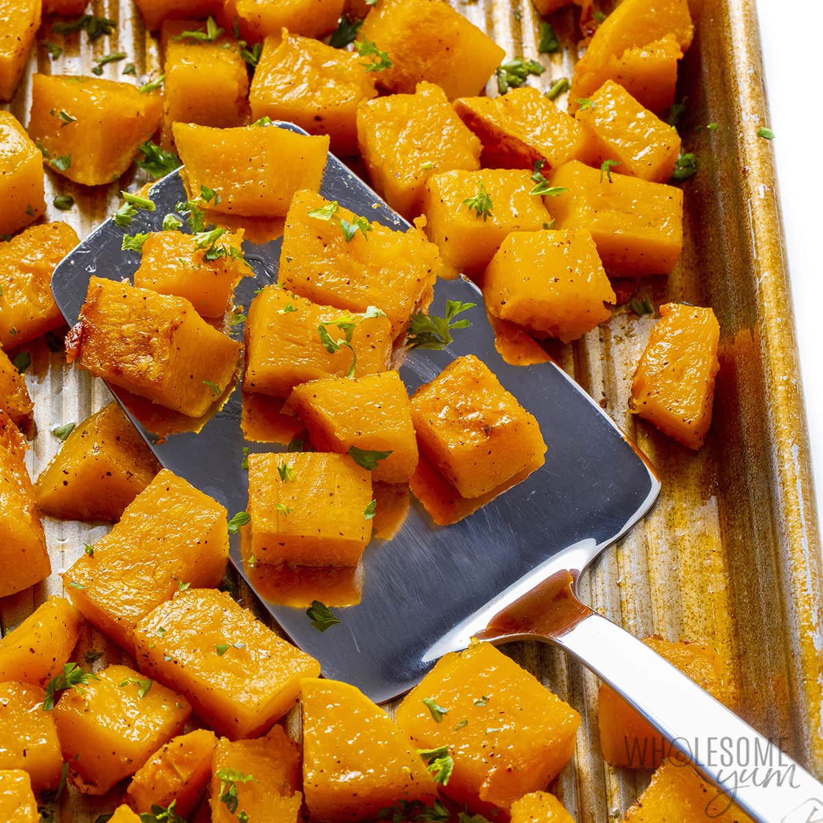Fully roasted butternut squash cubes in a pan with a spatula.
