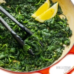 Sauteed spinach in skillet with tongs and lemon slices.