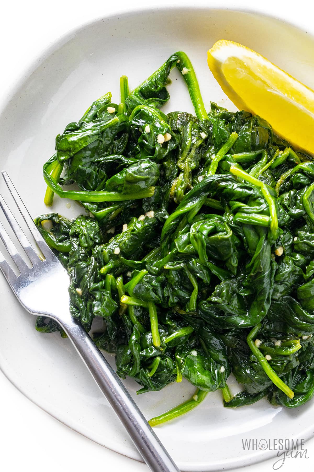 Sauteed spinach with garlic on a plate with a fork and a lemon.