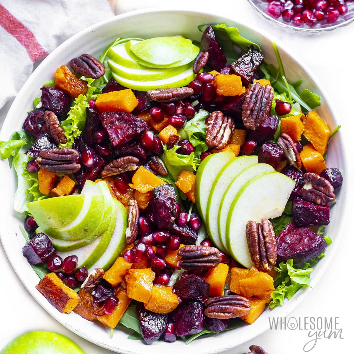 Greens, apples, butternut squash, beets, and pomegranate seeds in a bowl.