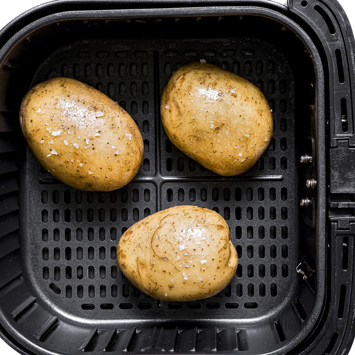 Potatoes seasoned in air fryer basket before cooking.