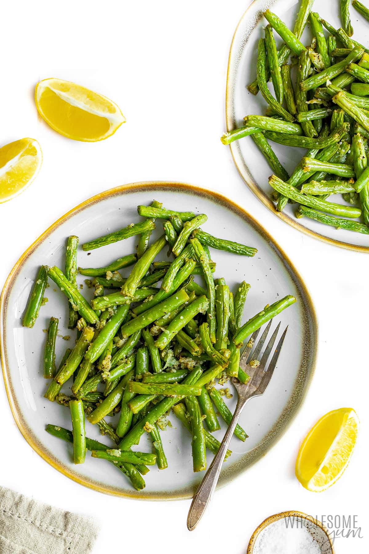 Green beans on two plates with scattered lemon wedges.