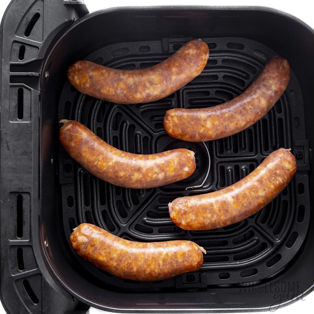 Raw sausage in air fryer basket.
