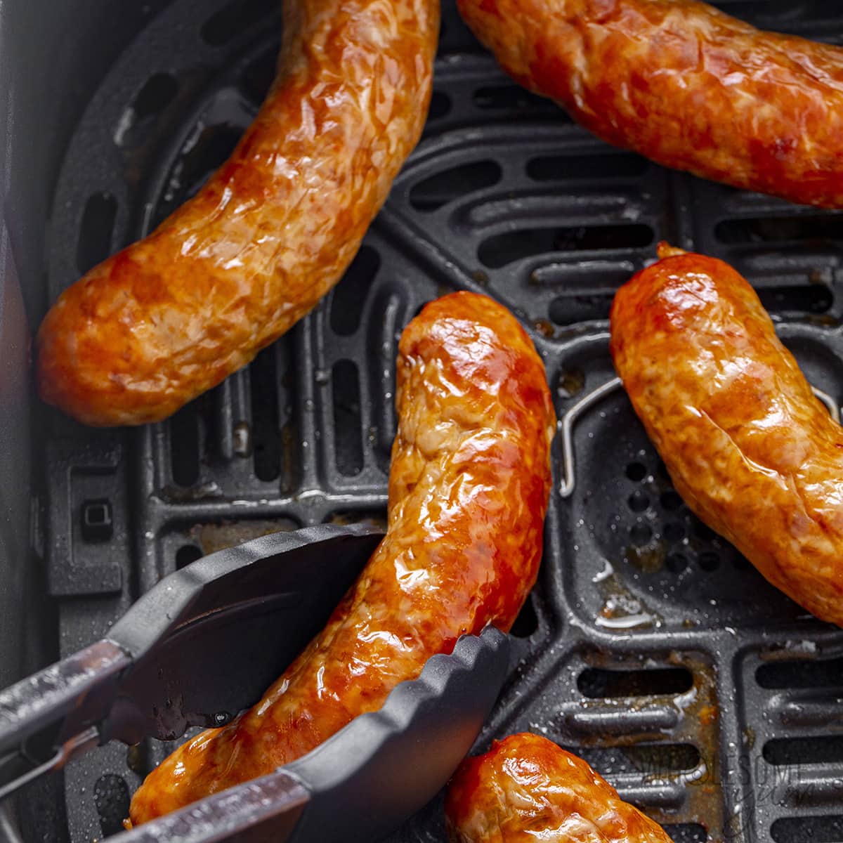 Use tongs to pick up the cooked air fryer sausage.