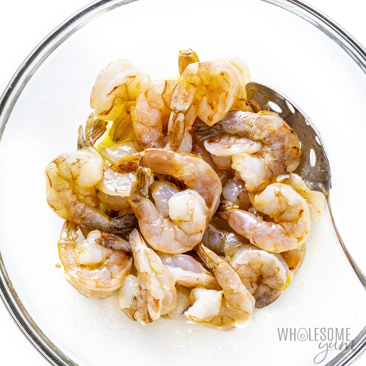 Raw shrimp tossed in oil in a bowl.