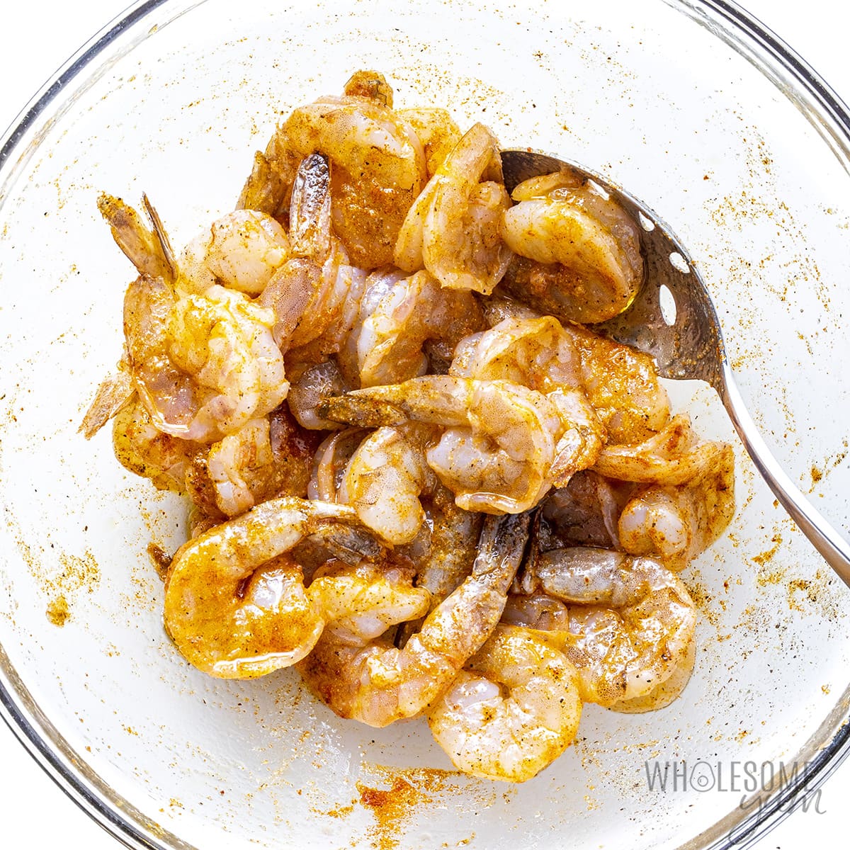 Raw shrimp tossed with seasonings in a bowl.