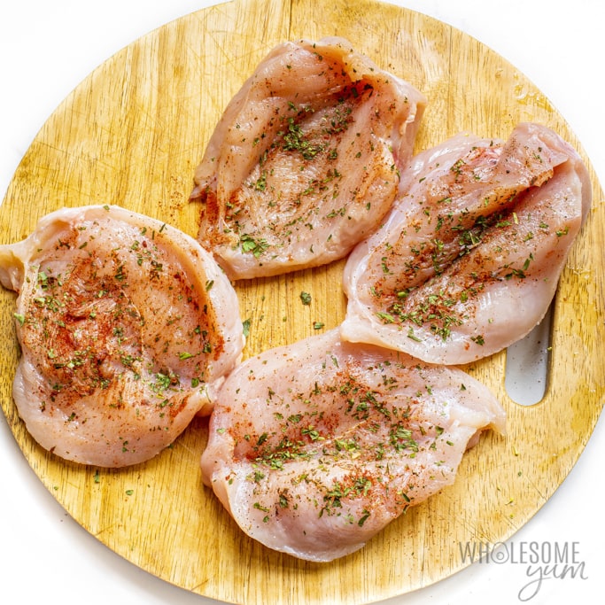 Chicken seasoned with herbs and spices on cutting board.