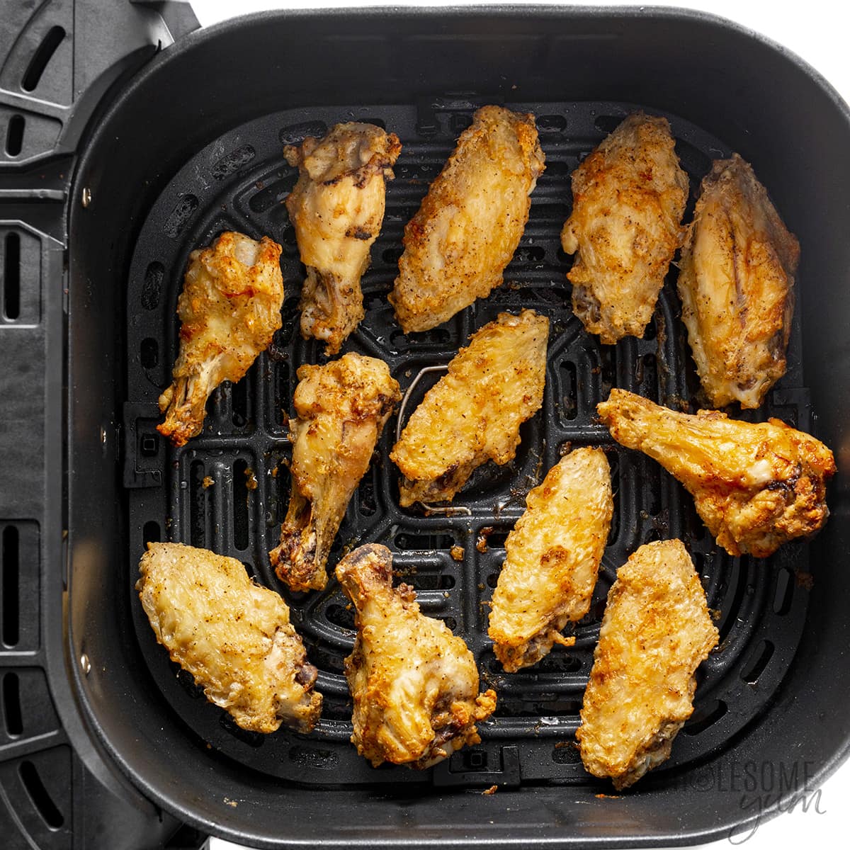 Crispy chicken wings in an air fryer basket.