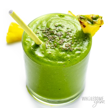 Glass of green detox smoothie with a straw, chia seeds sprinkled on top and a pineapple wedge garnish.