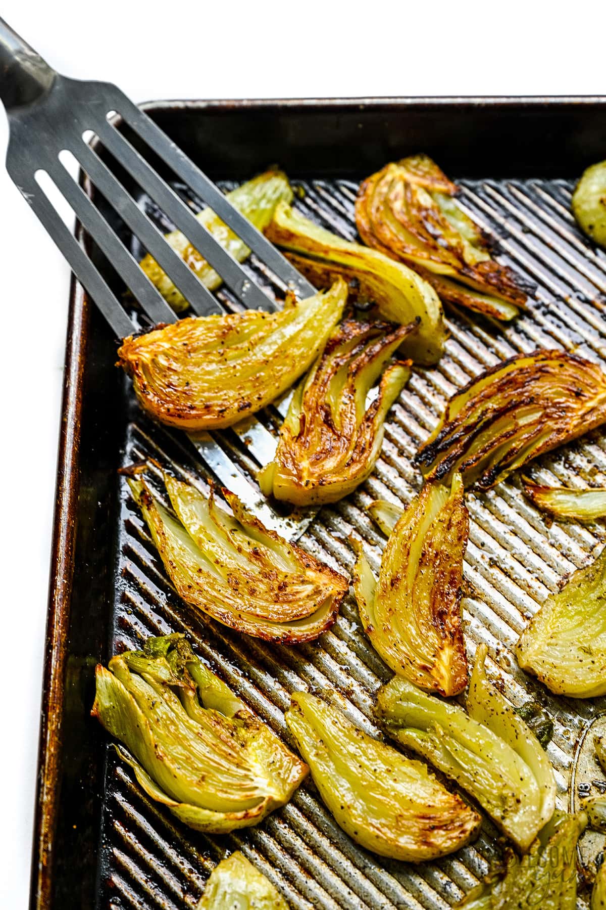 Roasted fennel on a sheet pan with a spatula. 