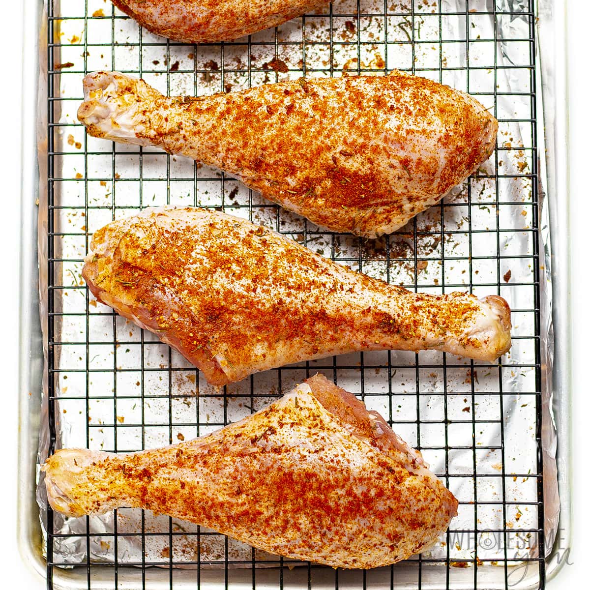 Poultry sprinkled with spices on baking rack.