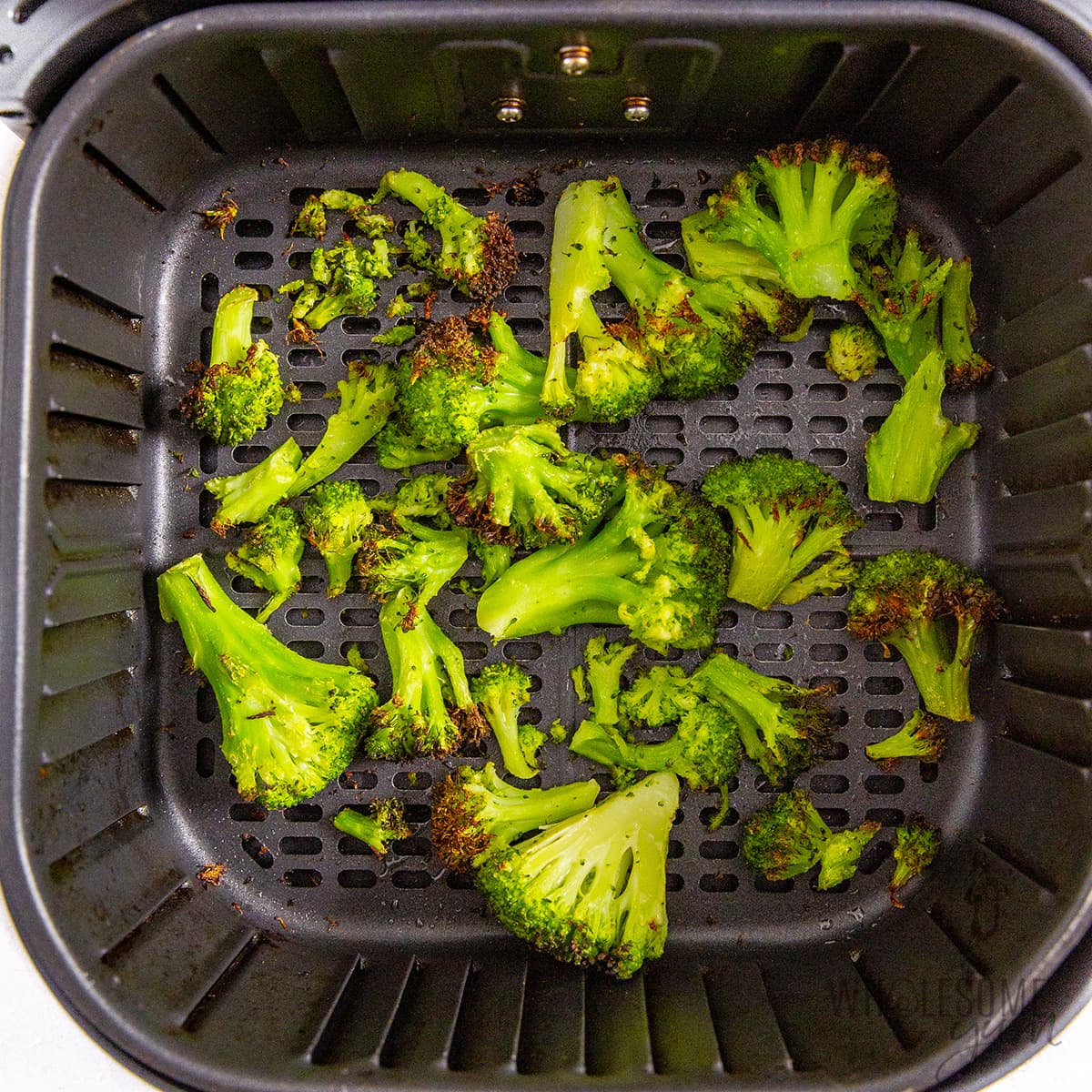 Cooked frozen broccoli in air fryer basket.