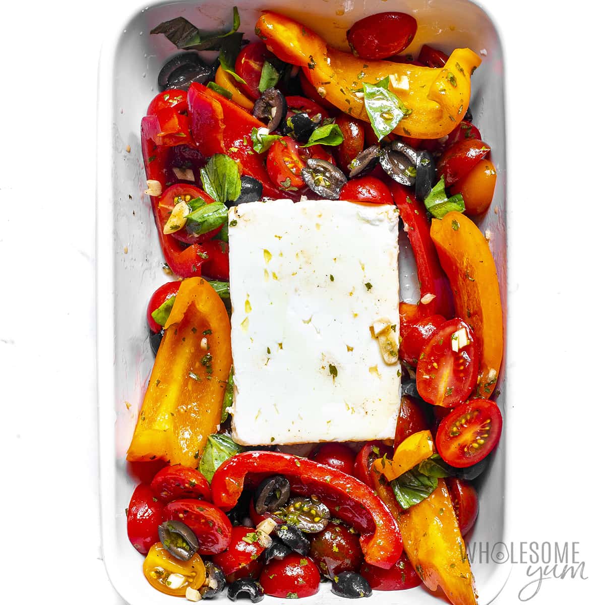 Feta cheese in the center of baking dish surrounded by veggies.