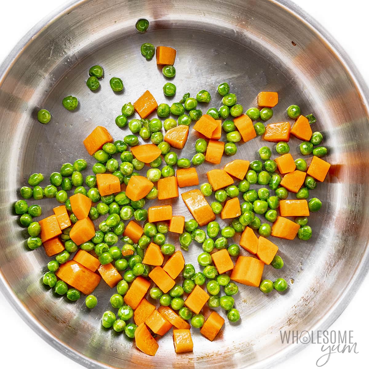 Sauteed peas and carrots in a skillet.