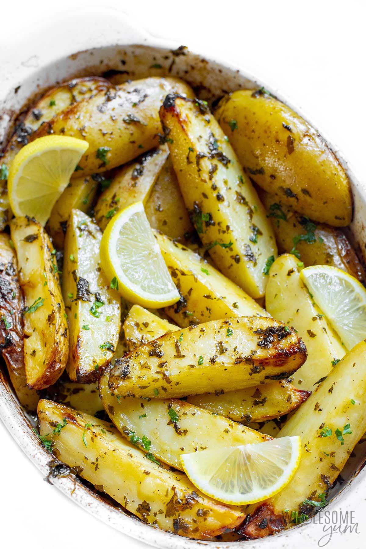 Greek lemon potatoes in baking dish with lemon wedges.
