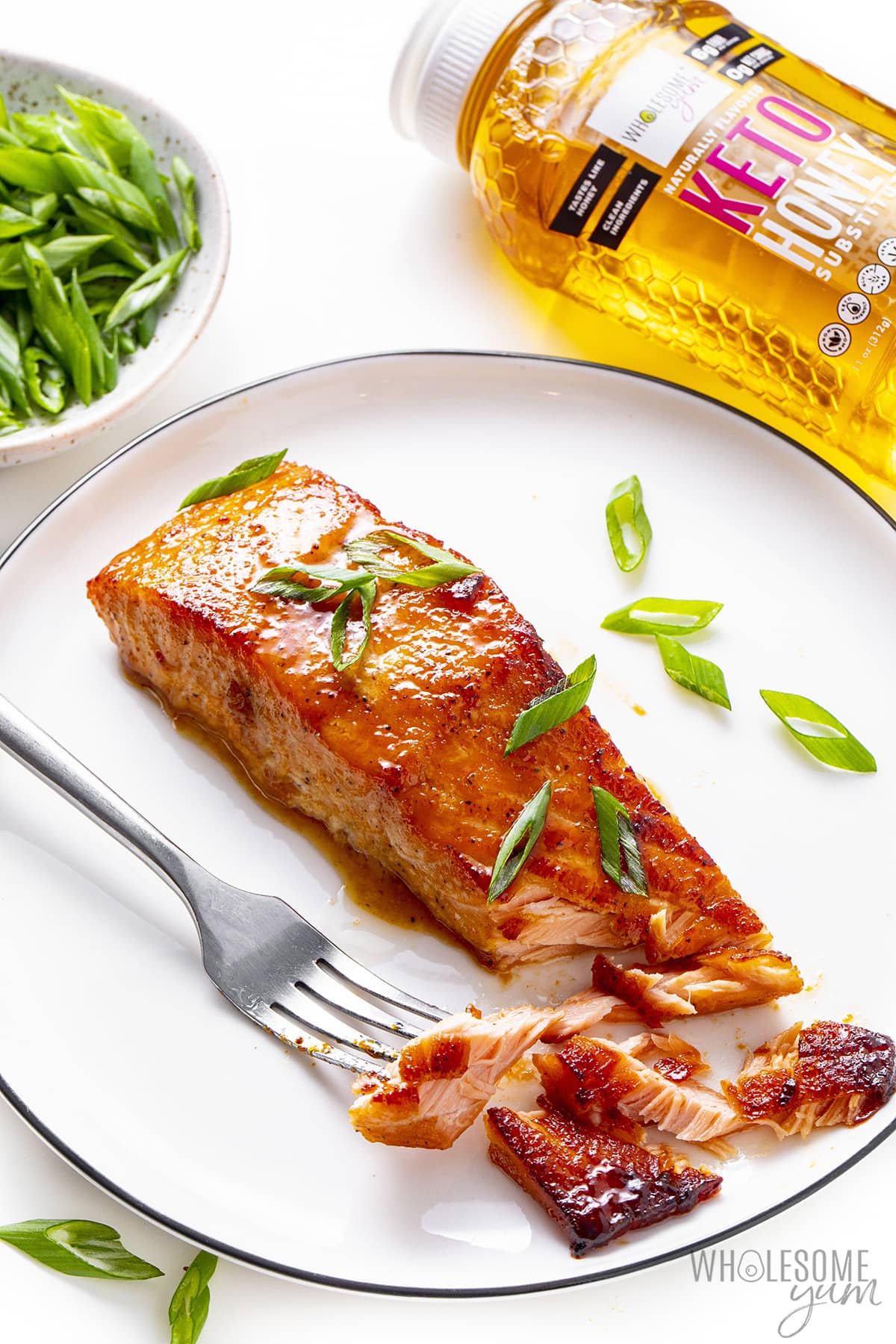 Keto salmon on a plate with a fork next to Wholesome Yum Honey.