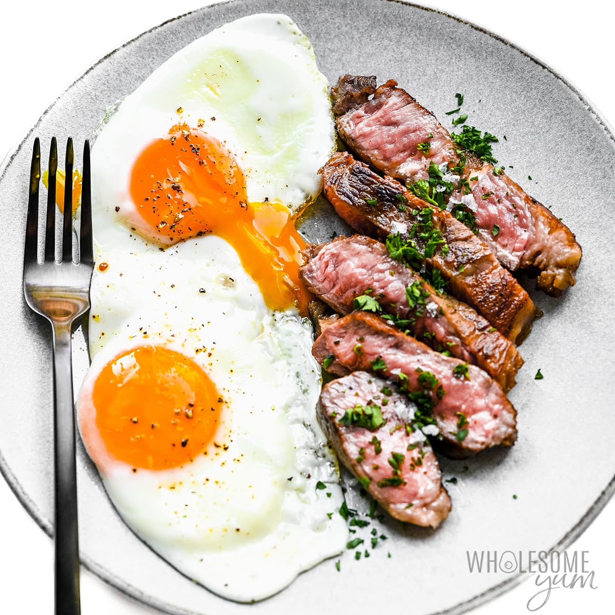 Sunny side up eggs and sliced steak on a plate.