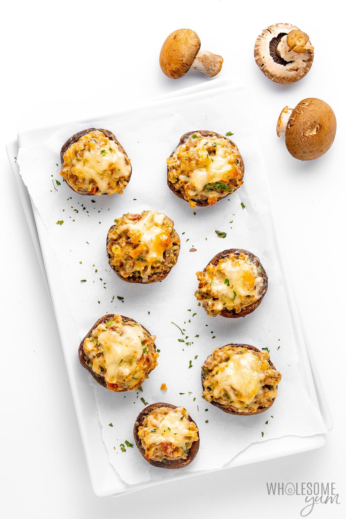 Stuffed mushrooms arranged on parchment paper and sprinkled with parsley.